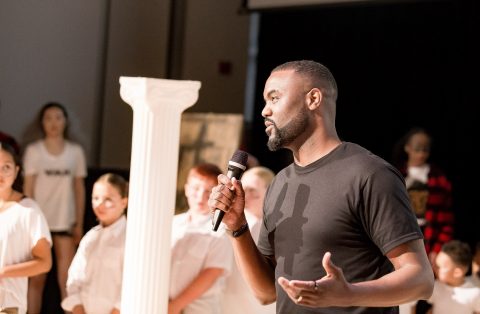 NSCAD alumni Duane Jones speaks into a microphone, addressing a crowd of listeners.