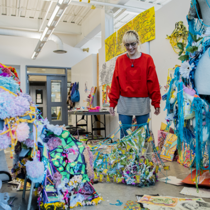 A person standing amongst their artwork, which is in the form of sculptures and wall art around them.