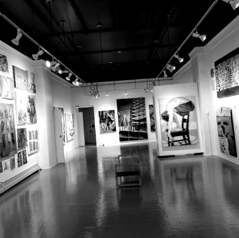 Black and white photo of multiple paintings hanging at the Anna Leonowens Gallery.