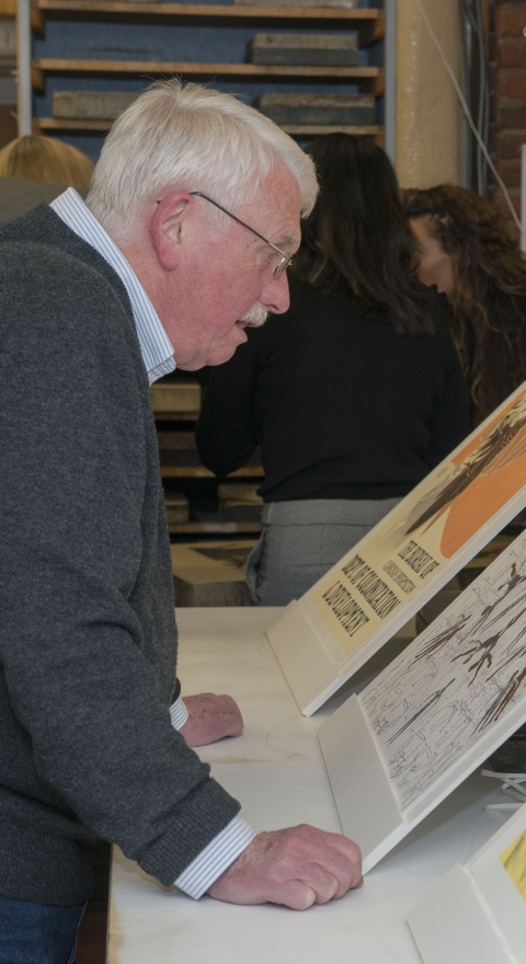 An older man with white hair looking at prints displayed on a table.