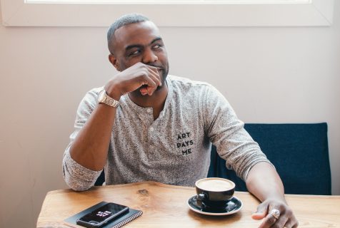 NSCAD alumni Duane Jones sitting, looking to his left, with a cup of coffee in front of him.