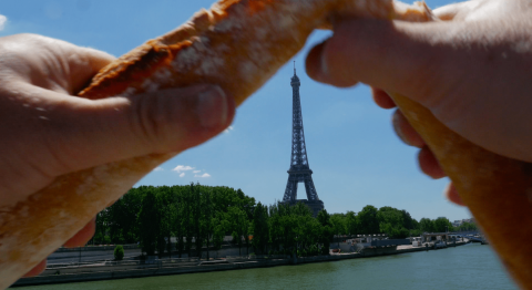 A baguette being broken with the Eiffel Tower in the background.
