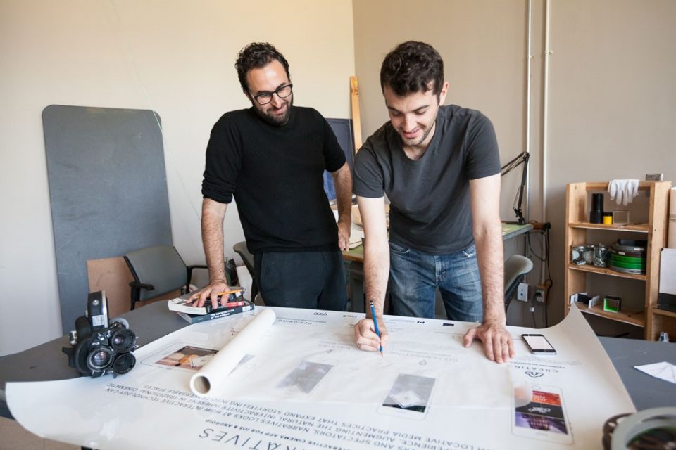 A film studies professor and a student look at a film's storyboard on a large desk 