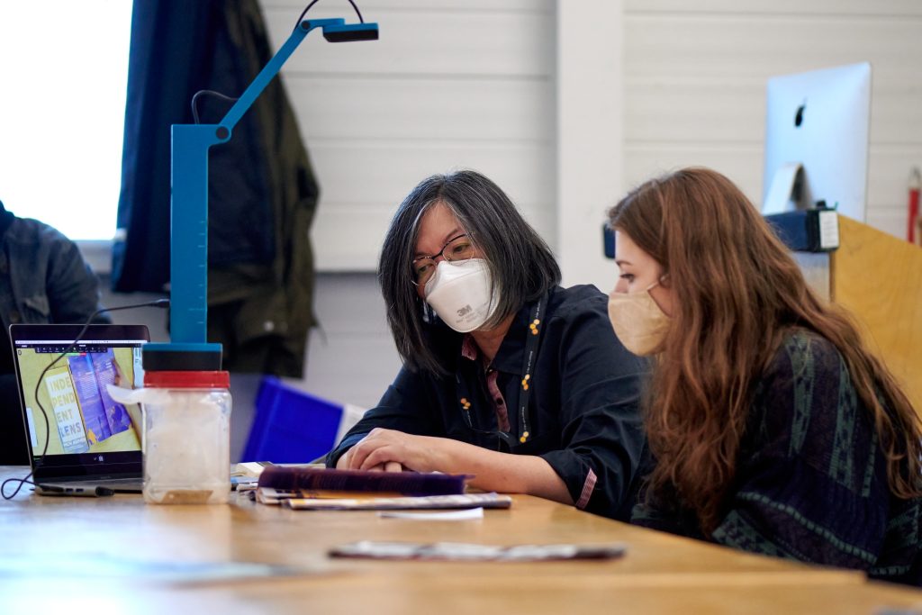 Student and professor looking at work on a desk.