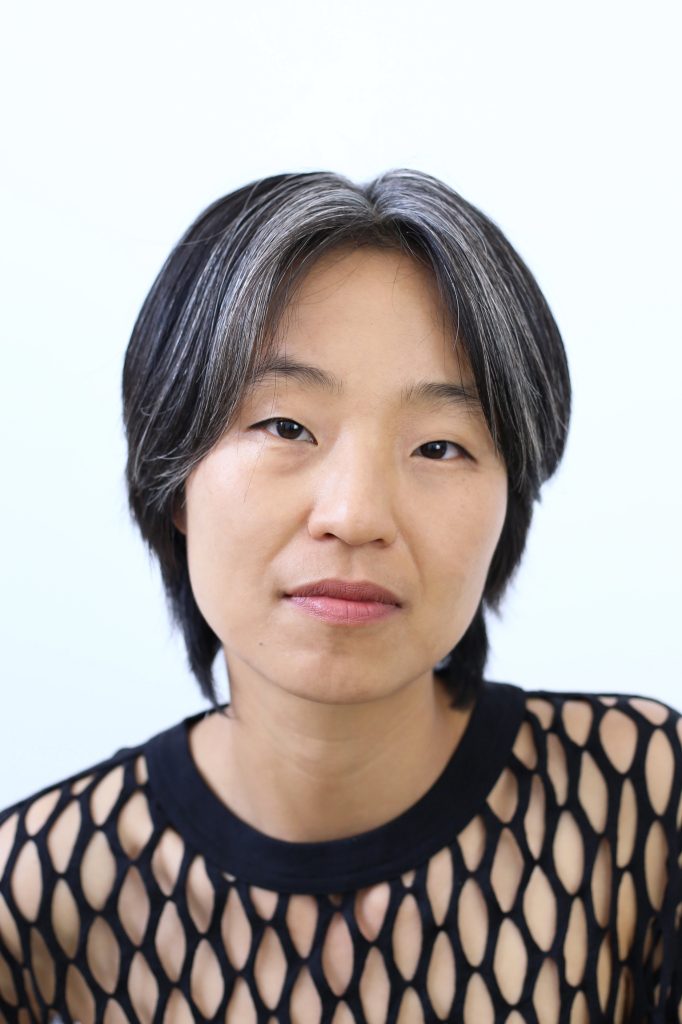 Headshot of woman with shoulder length dark and grey hair and black lace shirt.