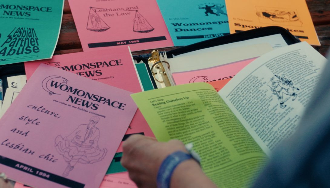 Hands flipping through many copies of Womonspace News zine.
