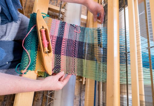 Hands at a loom weaving materials