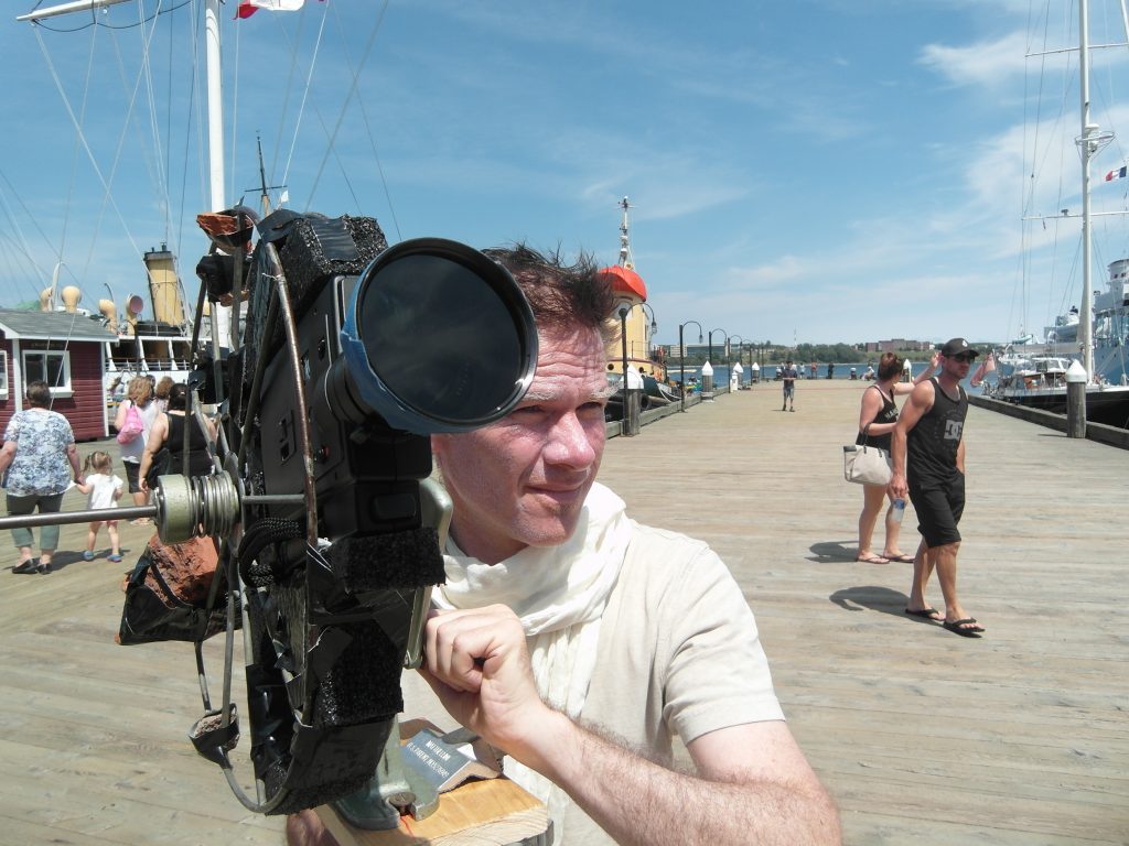 A white man in a white shirt operating a camera on the waterfront