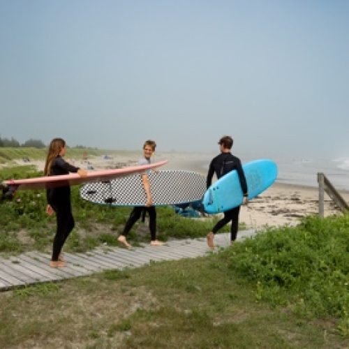 Surfers carrying their boards along a boardwalk to a foggy Nova Scotia beach