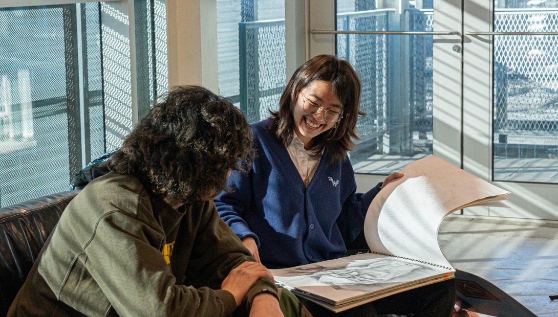 two people on a couch looking at a portfolio. Portfolio Day Winter 2025